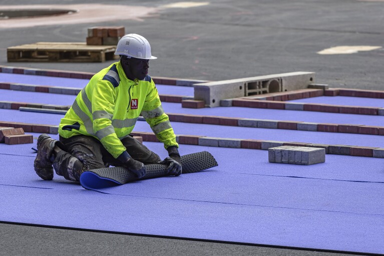 A worker rolls up the purple athletics track at the Olympic Stadium, currently known as Stade de France, in Saint-Denis, north of Paris, Tuesday, April 9, 2024. The Olympic Stadium will host the athletics events at the Paris 2024 Olympic Games. (AP Photo/Aurelien Morissard)